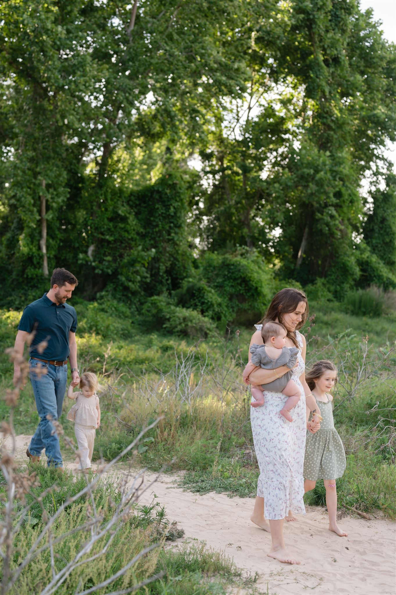 Family taking a stroll together on a sandy path through lush green trees and naturalized landscaping on a summer day.
