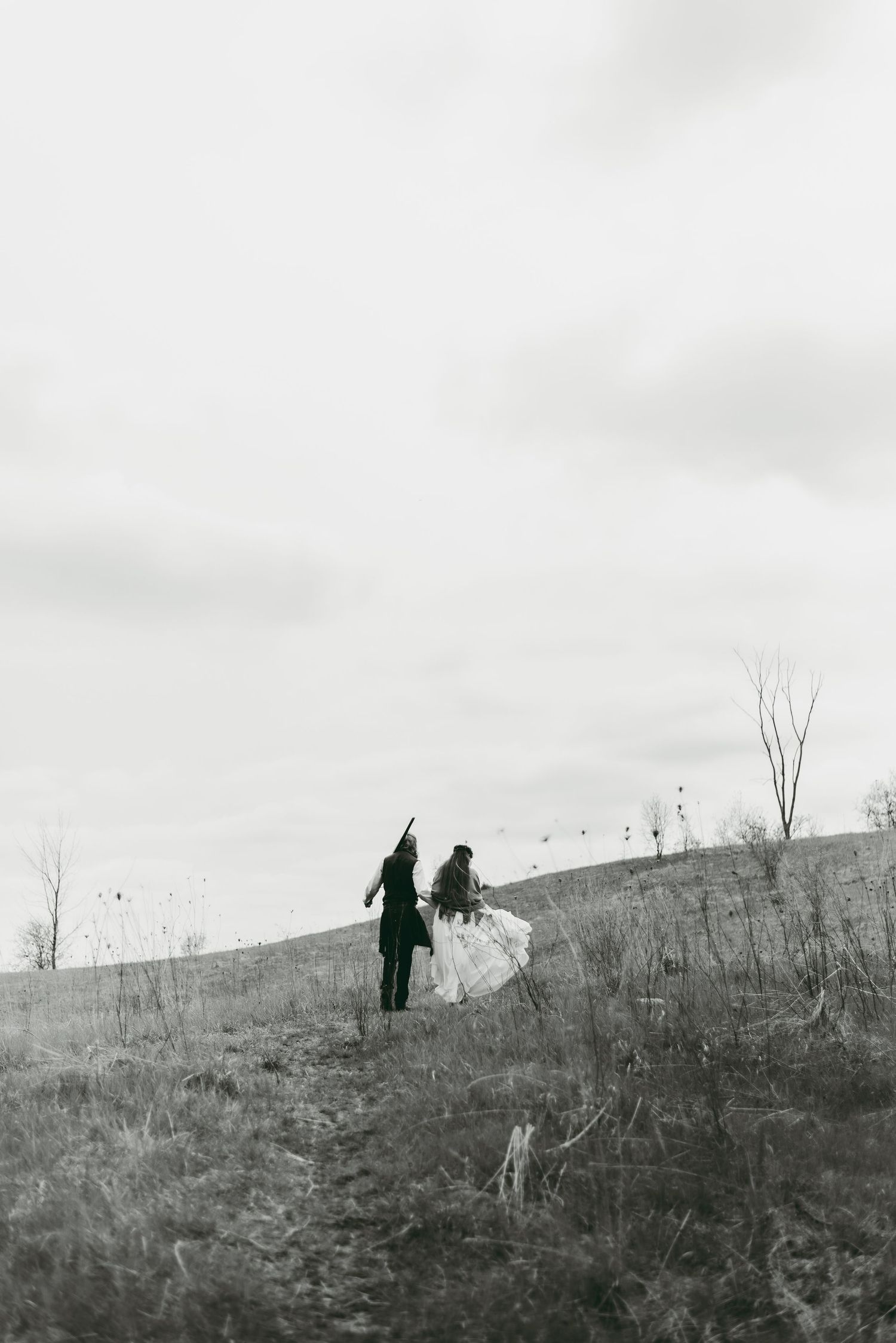 Bride and groom running through the fields in a cloudy forest clearing.