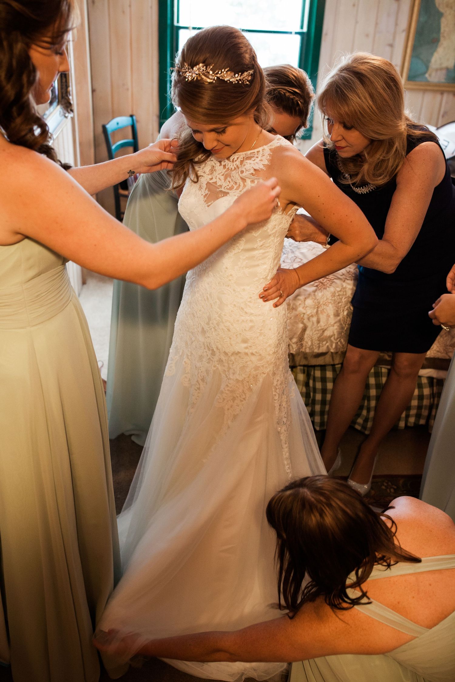 A group helps dress a bride in a lace wedding gown during wedding day preparations.