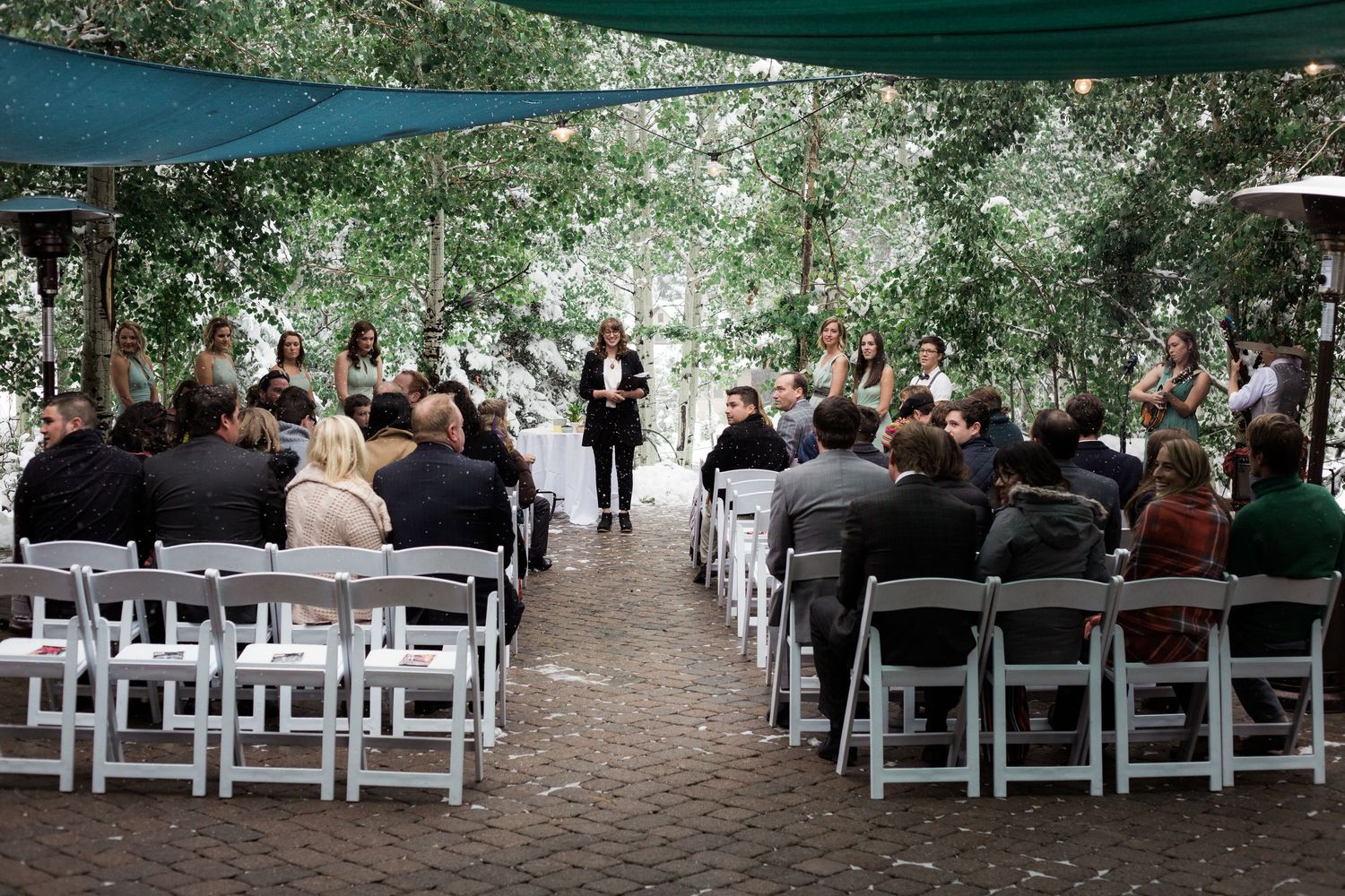 Outdoor wedding ceremony setup with white chairs and green canopy in a garden setting.