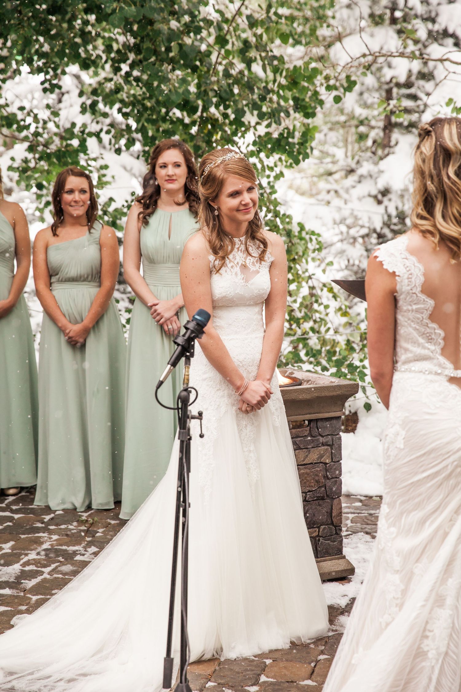 Bridesmaids in sage green dresses stand beside the bride during an outdoor wedding ceremony.