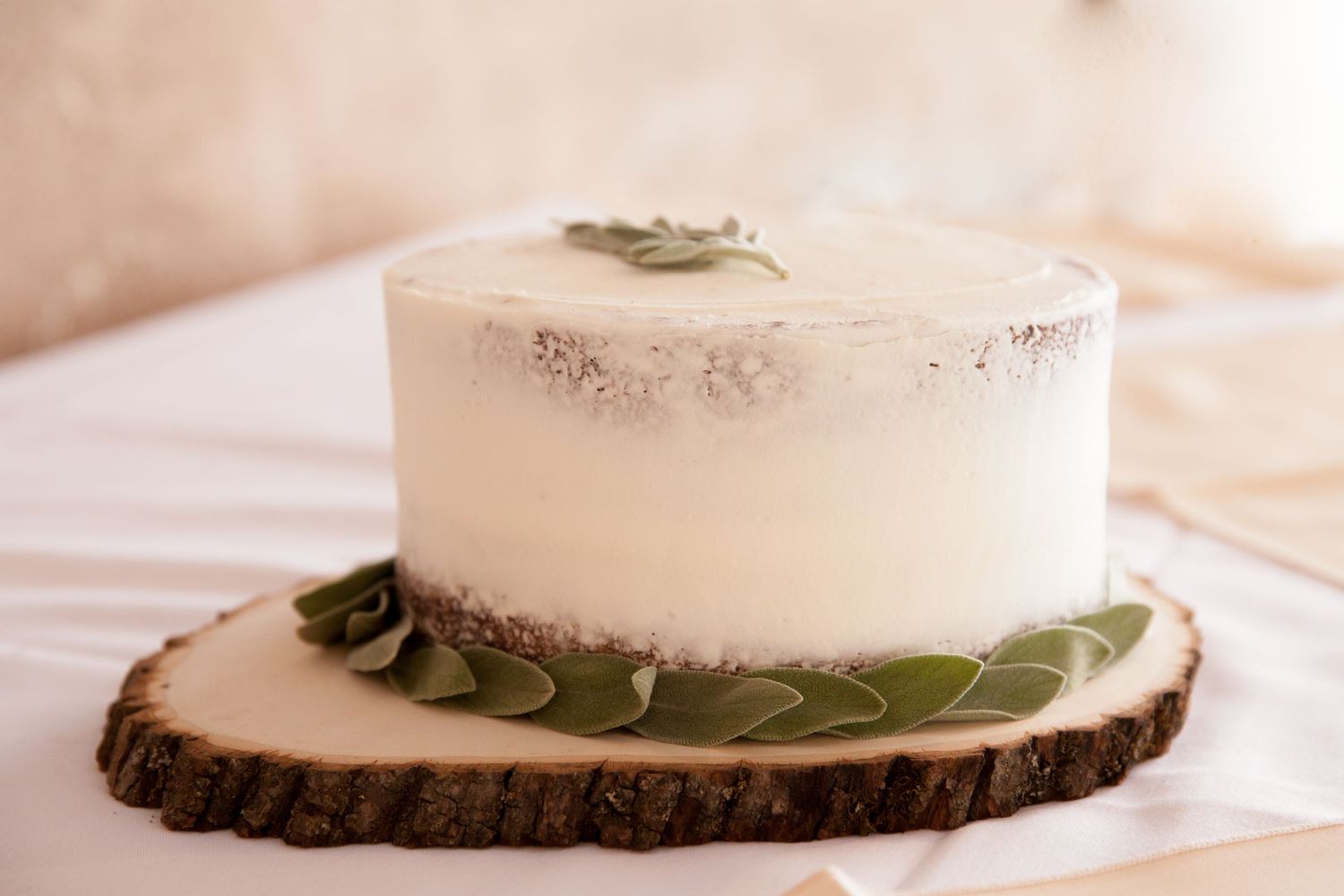 Single tier white frosted cake with green leaf decorations displayed on a rustic wood slice cake stand.