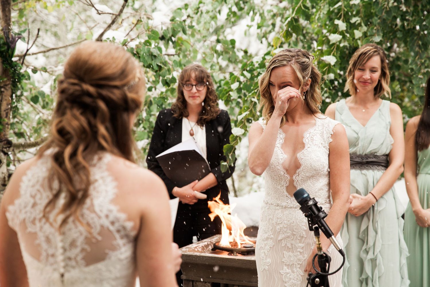 An emotional wedding ceremony takes place outdoors with bridesmaids in mint green dresses watching the tearful moment.