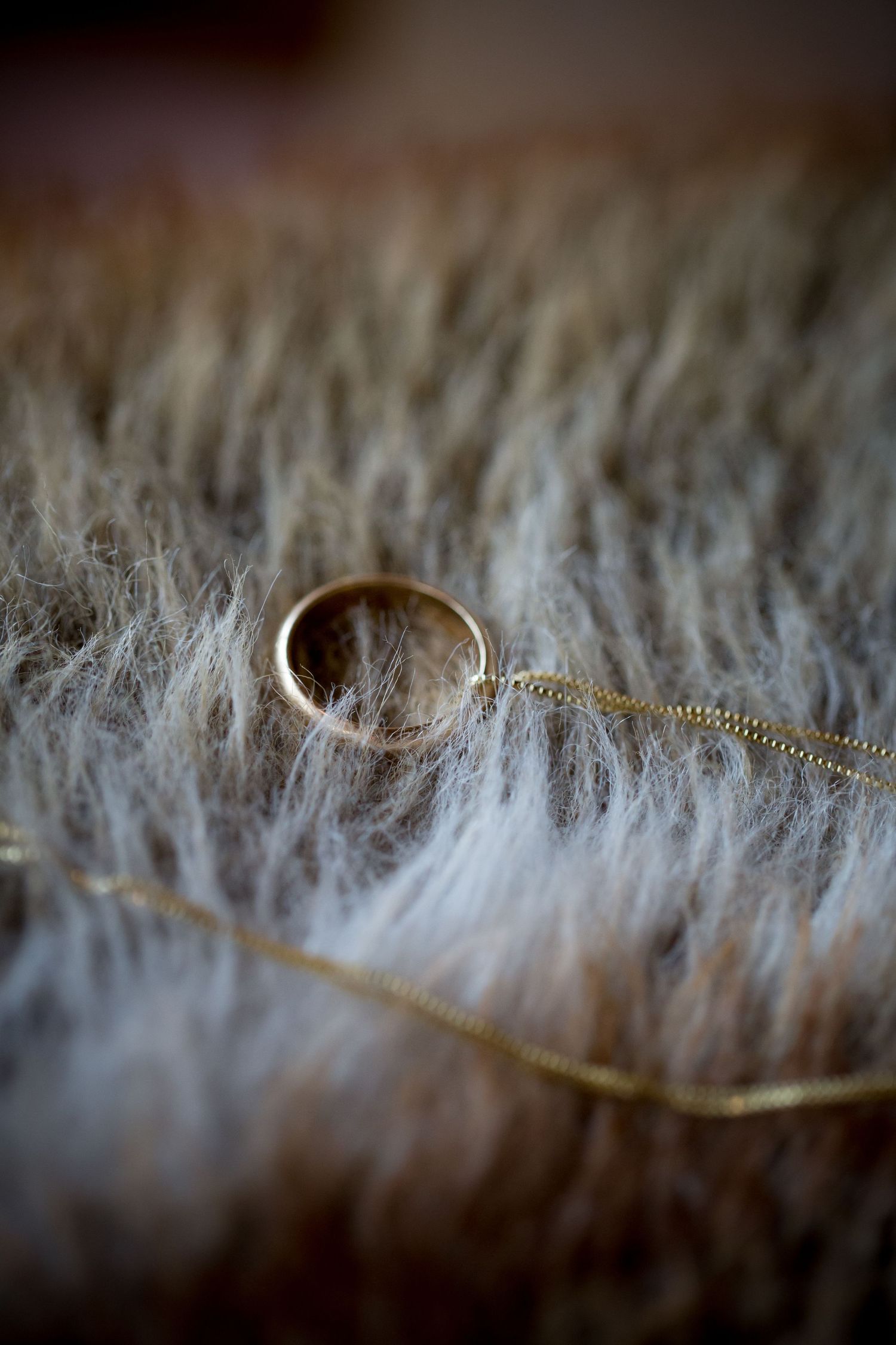 Gold wedding ring and delicate chain necklace artistically photographed against soft fuzzy textured fabric background.