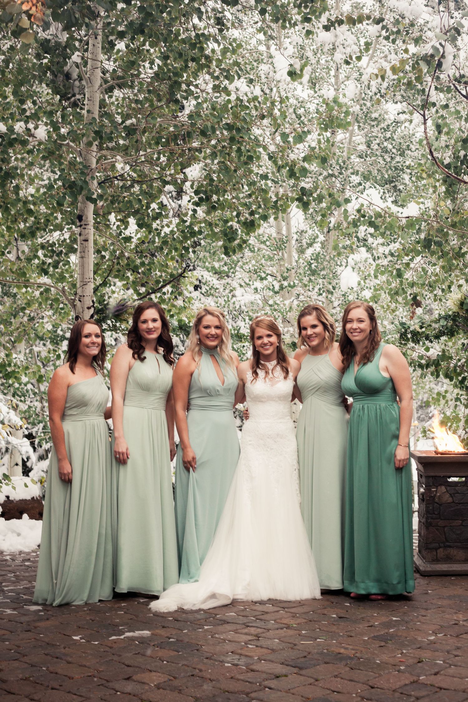 Wedding party poses outdoors wearing sage green and mint bridesmaid dresses with a bride in white on brick patio.