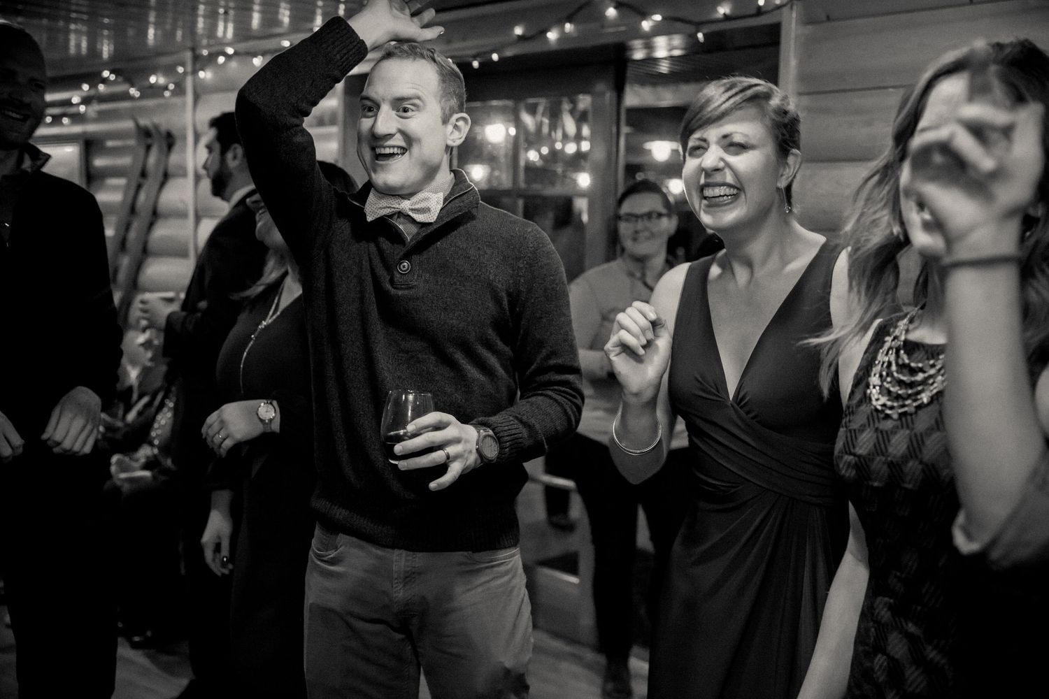 Party guests laughing and celebrating at an indoor social gathering with string lights in the background.