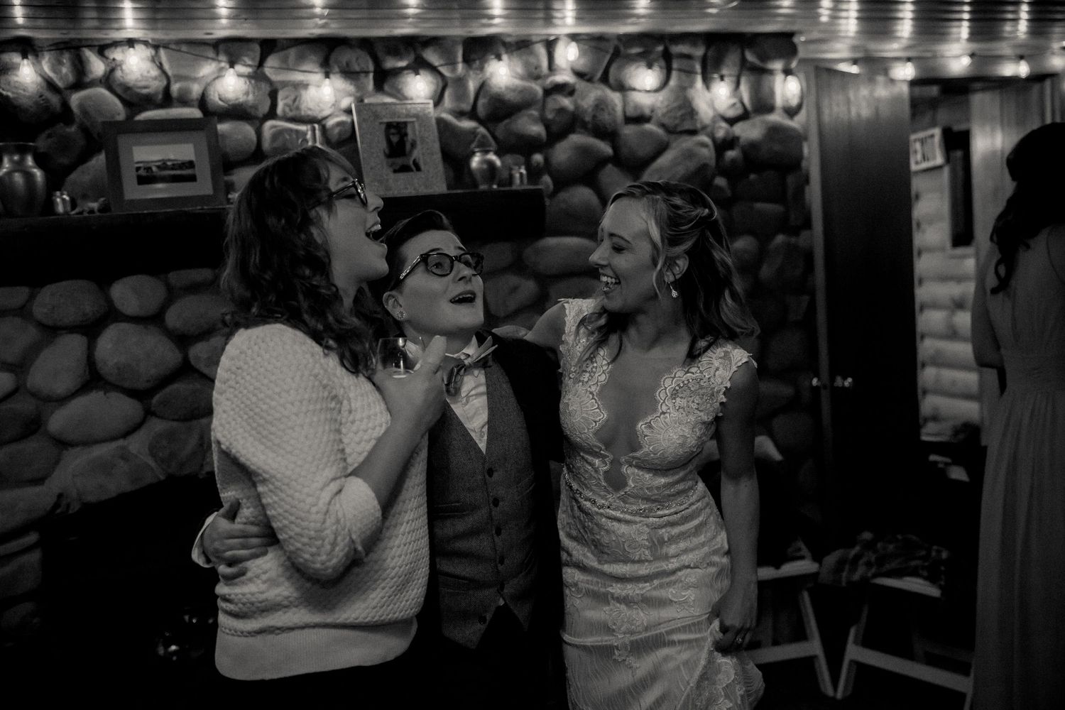 Black and white candid photo of party guests sharing joyful conversation in stone-walled venue.