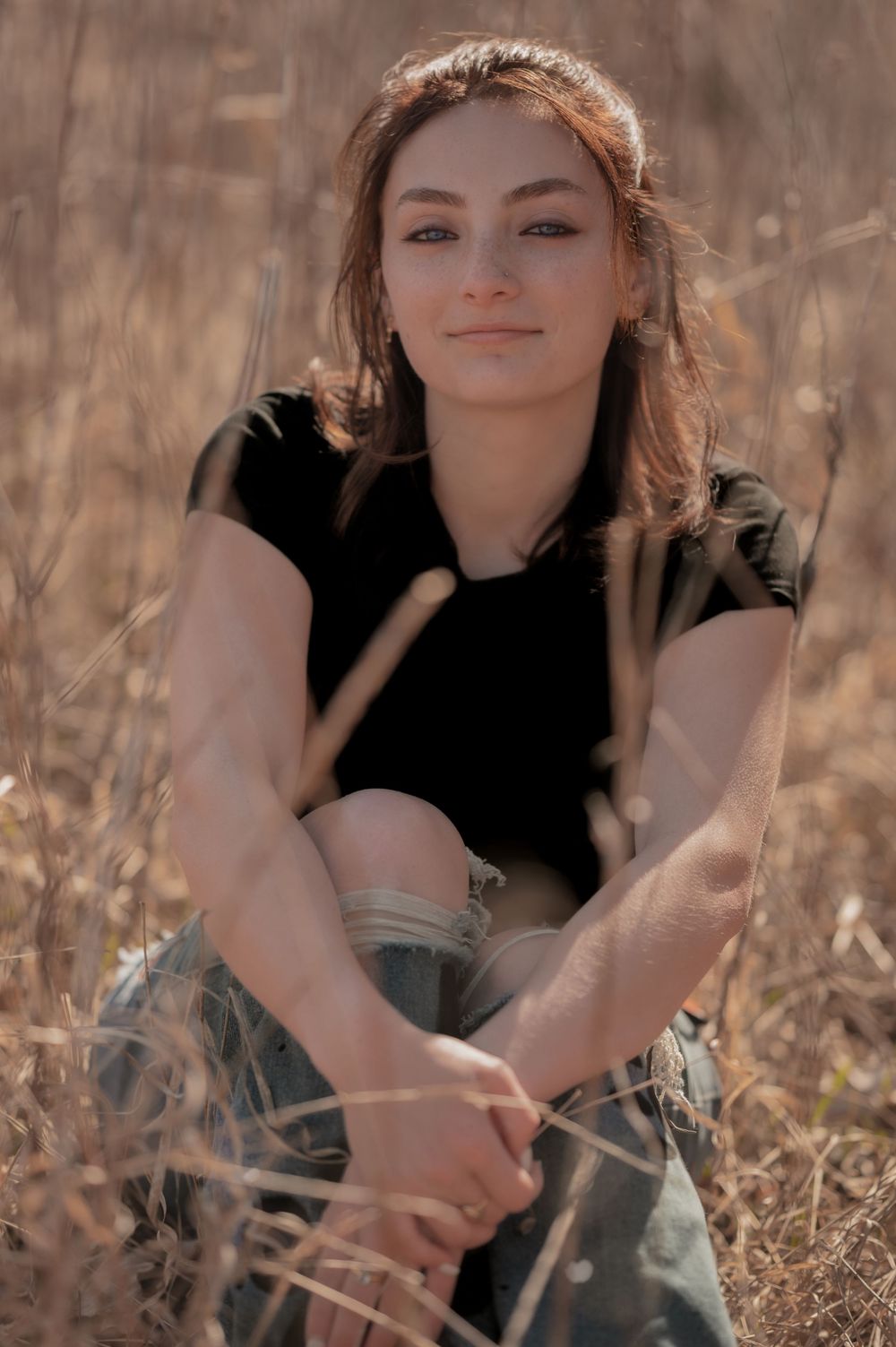 A dreamy outdoor portrait in warm tones features someone sitting casually among tall dried grasses.