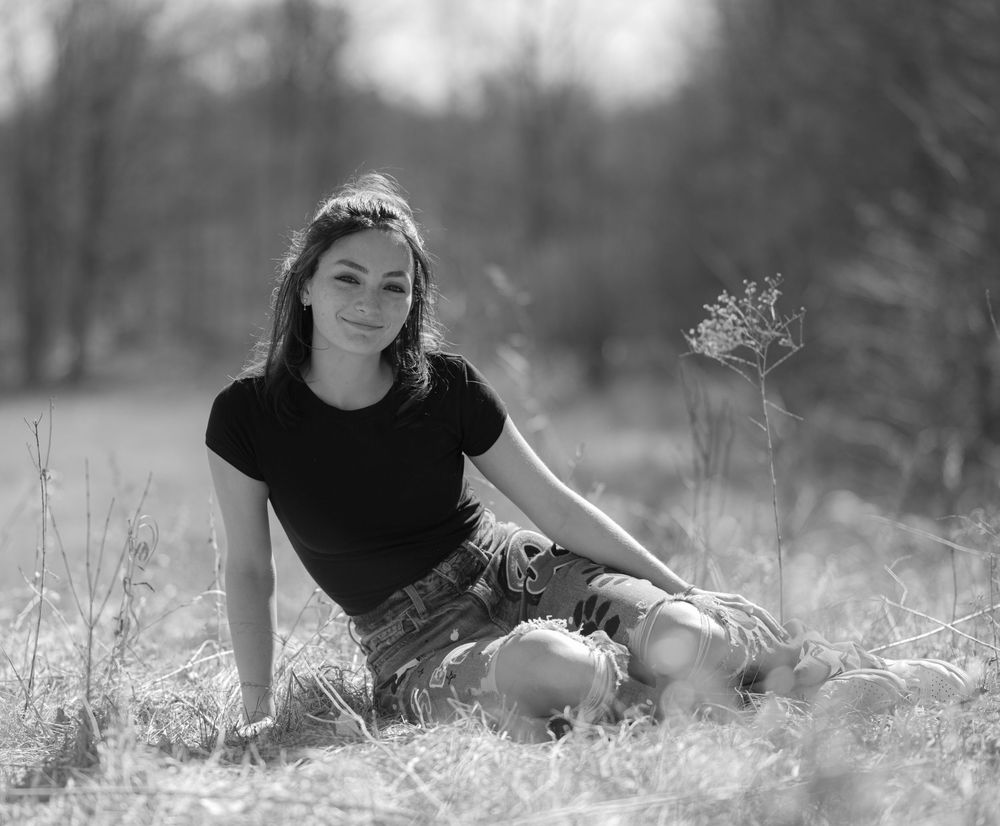 A person wearing a black top relaxes in a sunny meadow in a casual black and white photograph.