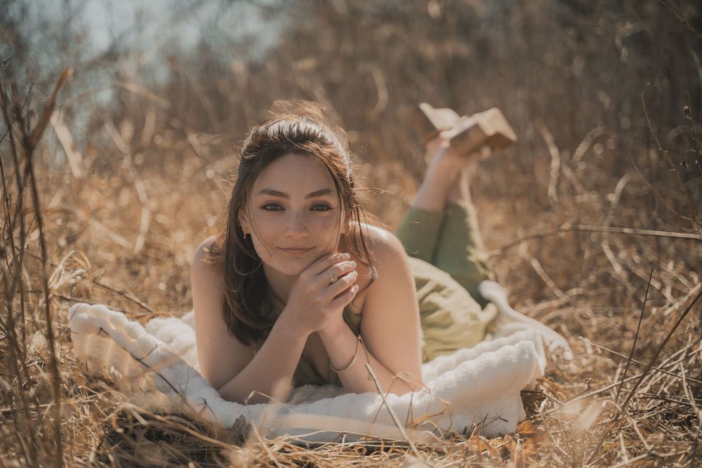 A person lies on a blanket in a golden field during sunset, creating a dreamy outdoor portrait.