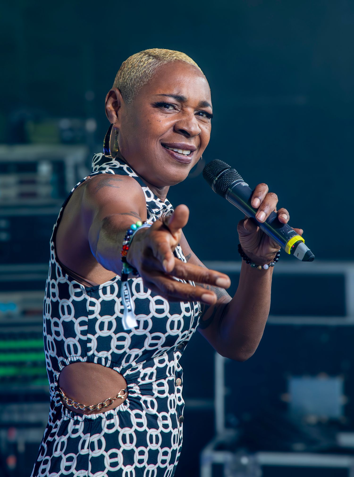 Performer in black and white patterned cutout dress sings energetically while holding microphone on stage.