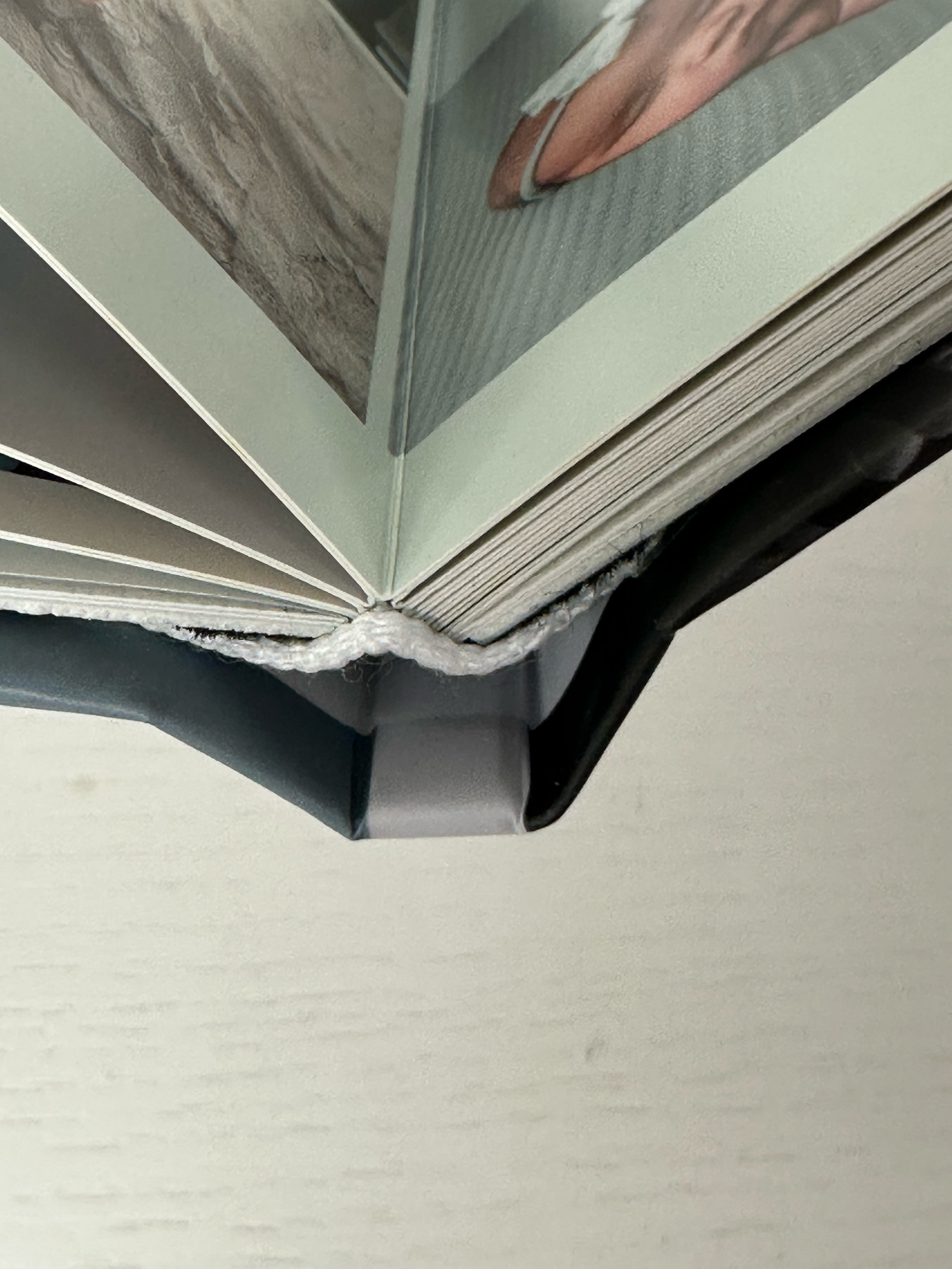Close-up of a photo book spine showing pages fanned open with a black cover and white binding detail. Photo book