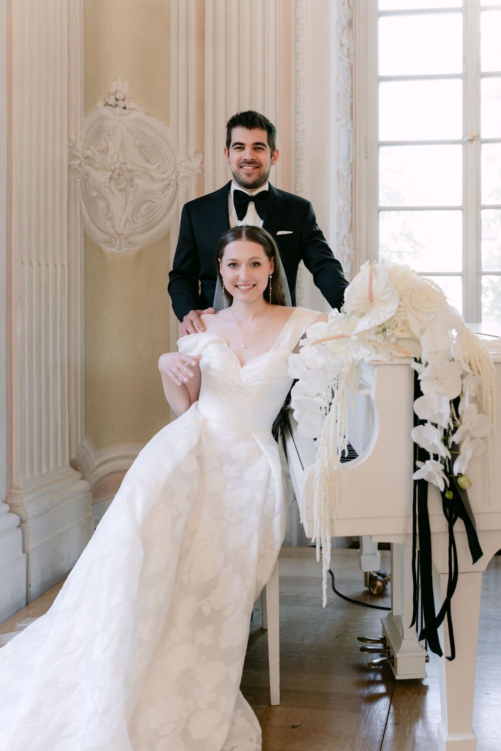 Elegant couple posing in a bright ornate room with white orchids and classical decor for their formal wedding portrait.