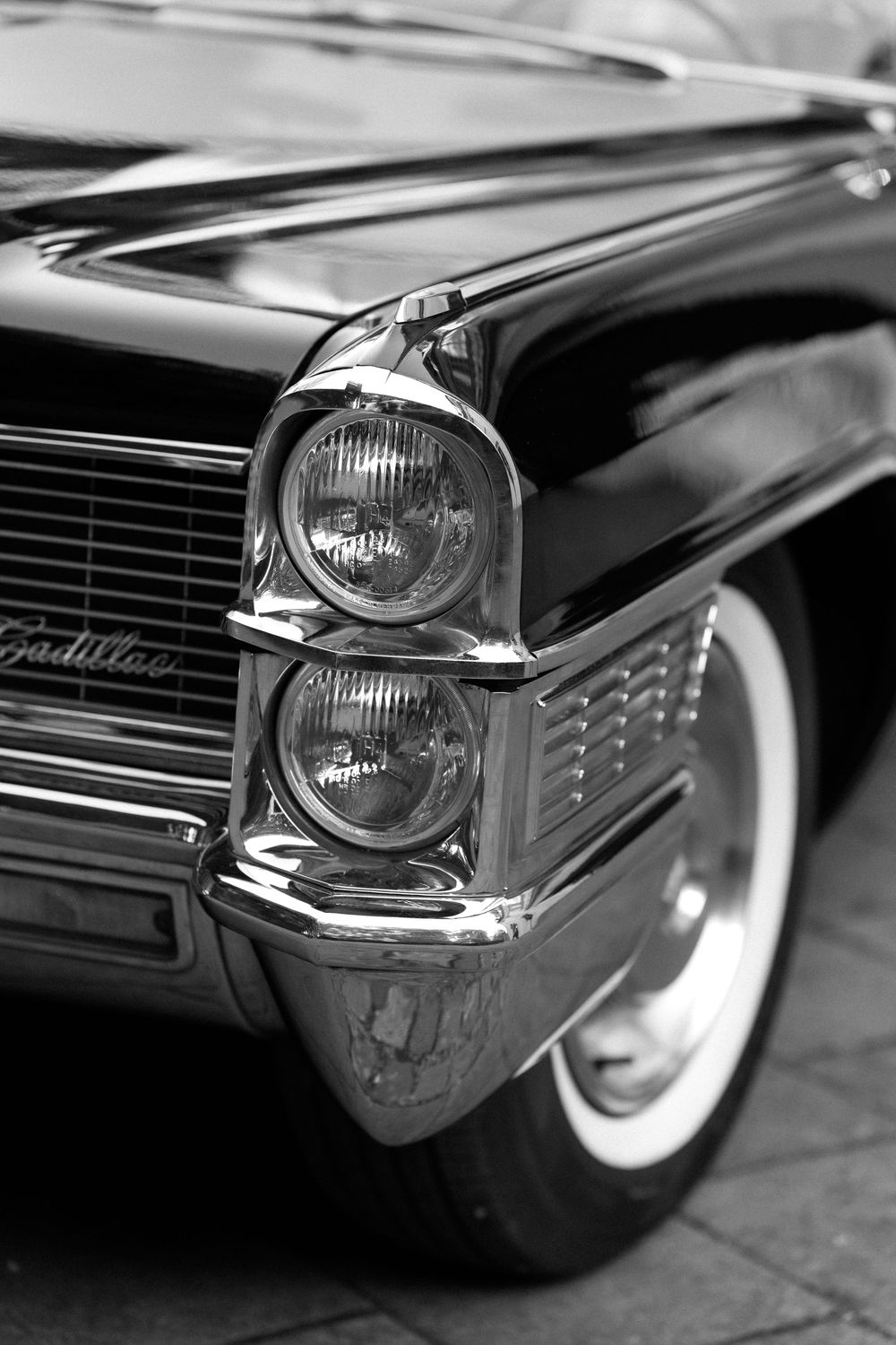 Classic Cadillac headlight and chrome grille detail shown in black and white photography with sleek vintage styling.