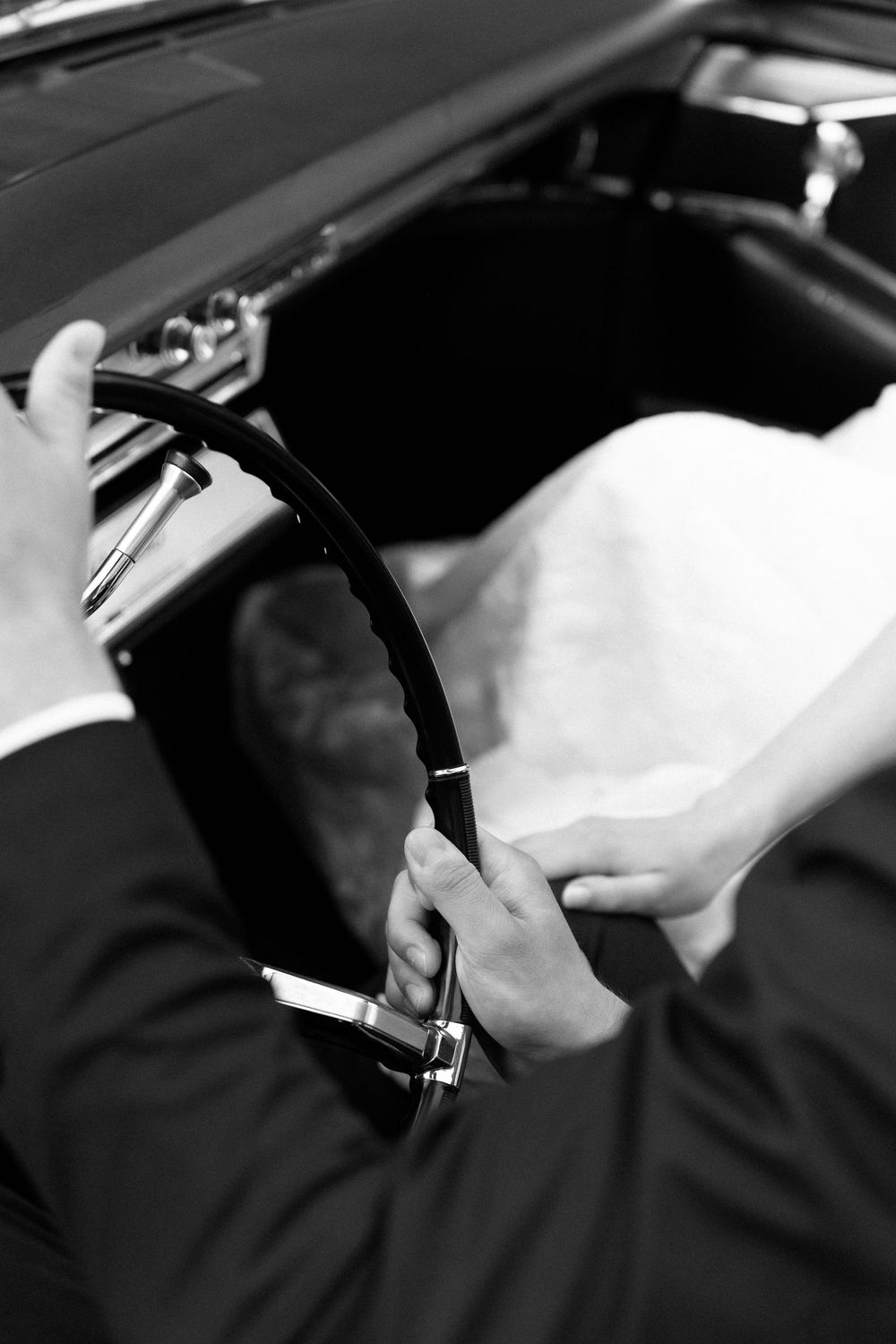 Black and white close-up of hands gripping a steering wheel in a car interior.