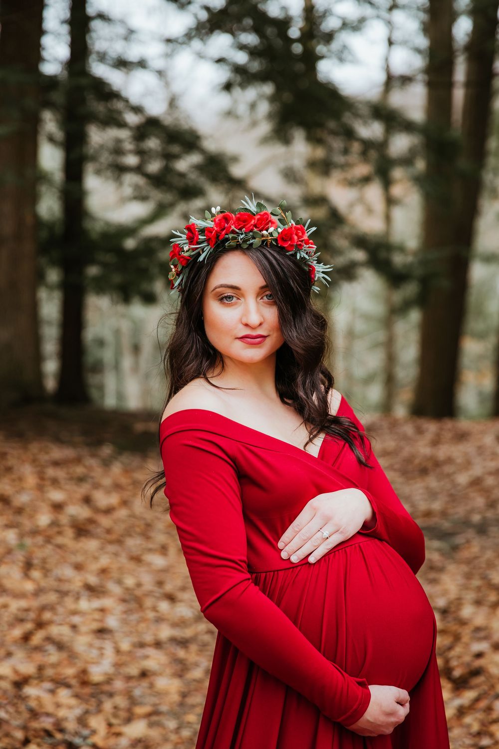 Ethereal maternity portrait featuring red gown and floral crown against forest backdrop.
