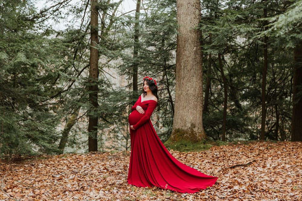 Side profile maternity shot with sweeping red dress train in forest setting.