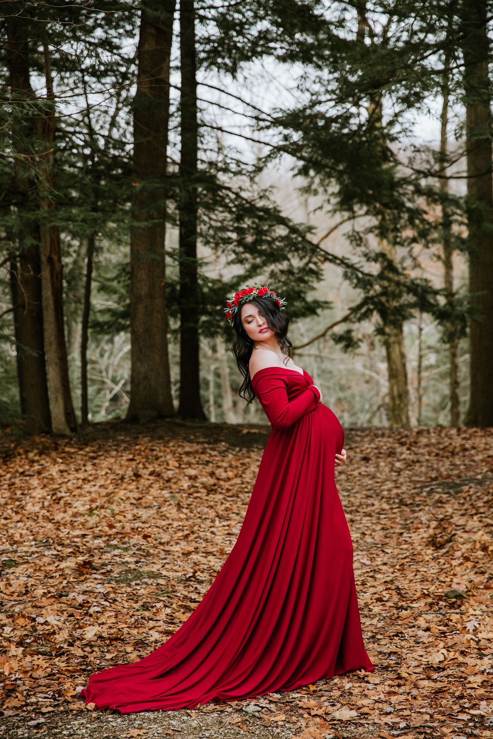 Stunning red dress cascades over autumn leaves in pine forest.