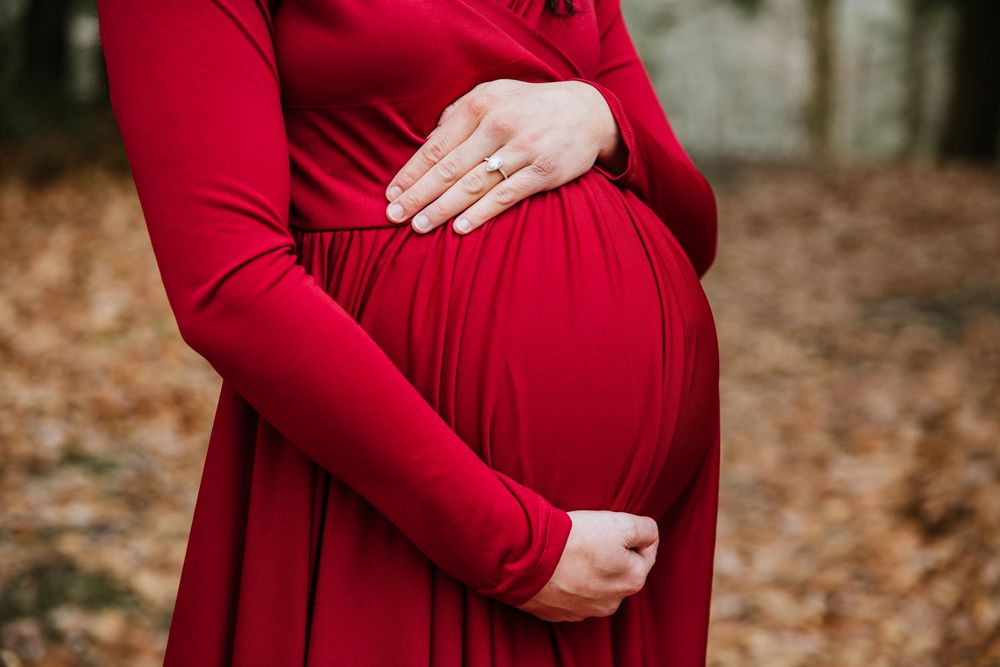 Close-up of hands cradling baby bump in flowing red maternity dress.