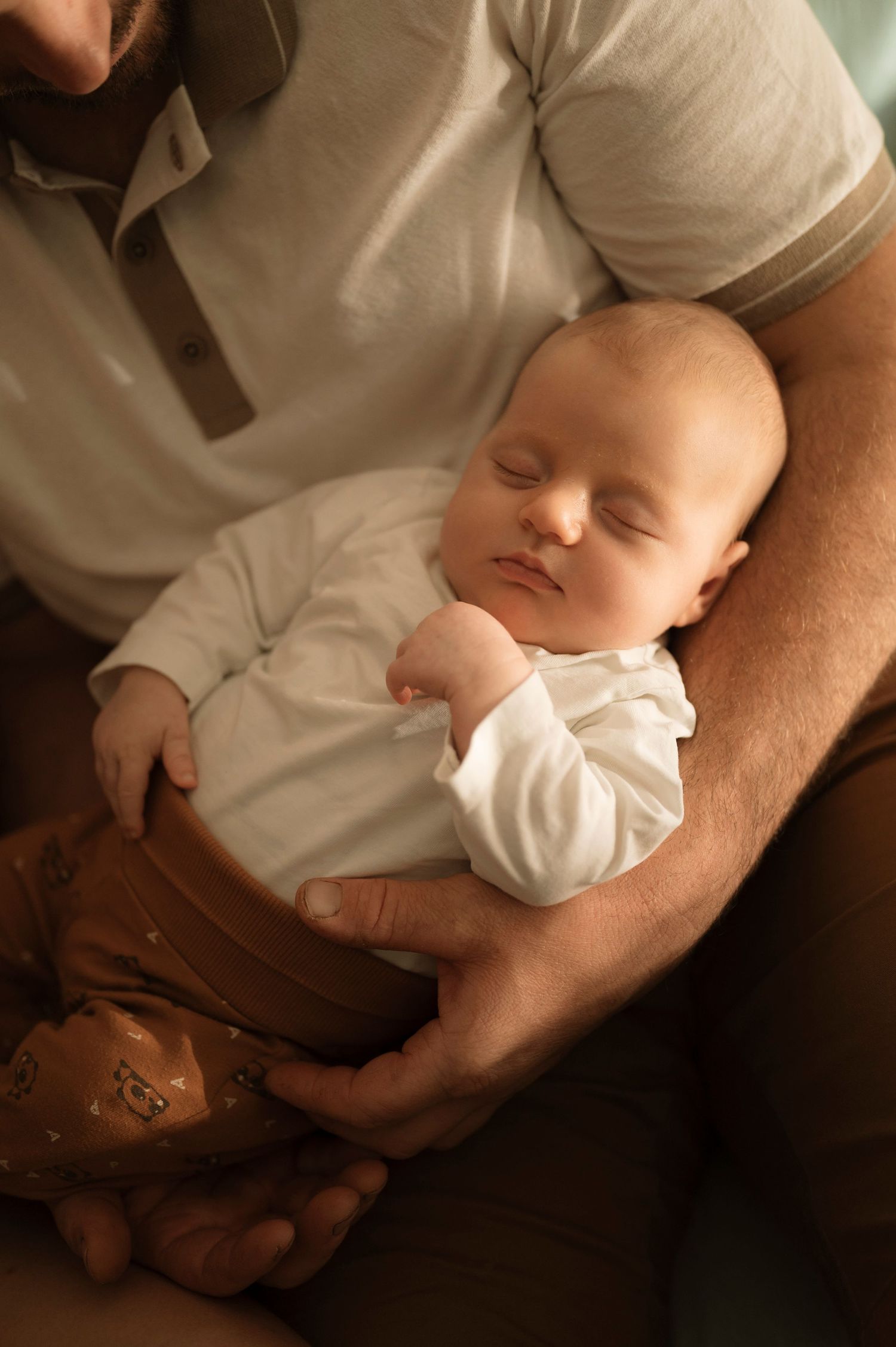 A sleeping baby in a white onesie resting peacefully in someone's arms.
