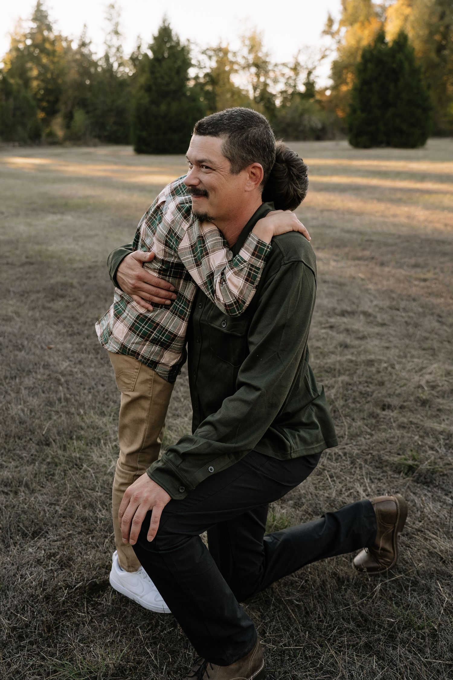 Emotional family portrait session capturing tender moments between family members in a field.