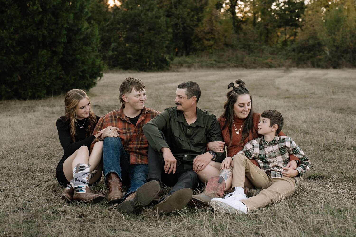 Family members lying together in a grassy field during a casual outdoor photo session.