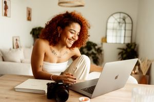Someone working on laptop at desk with coffee and plants in cozy home office setting.
