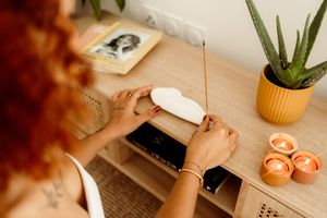 Hands opening white device on wooden desk with aloe plant and lit candles creating warm atmosphere.