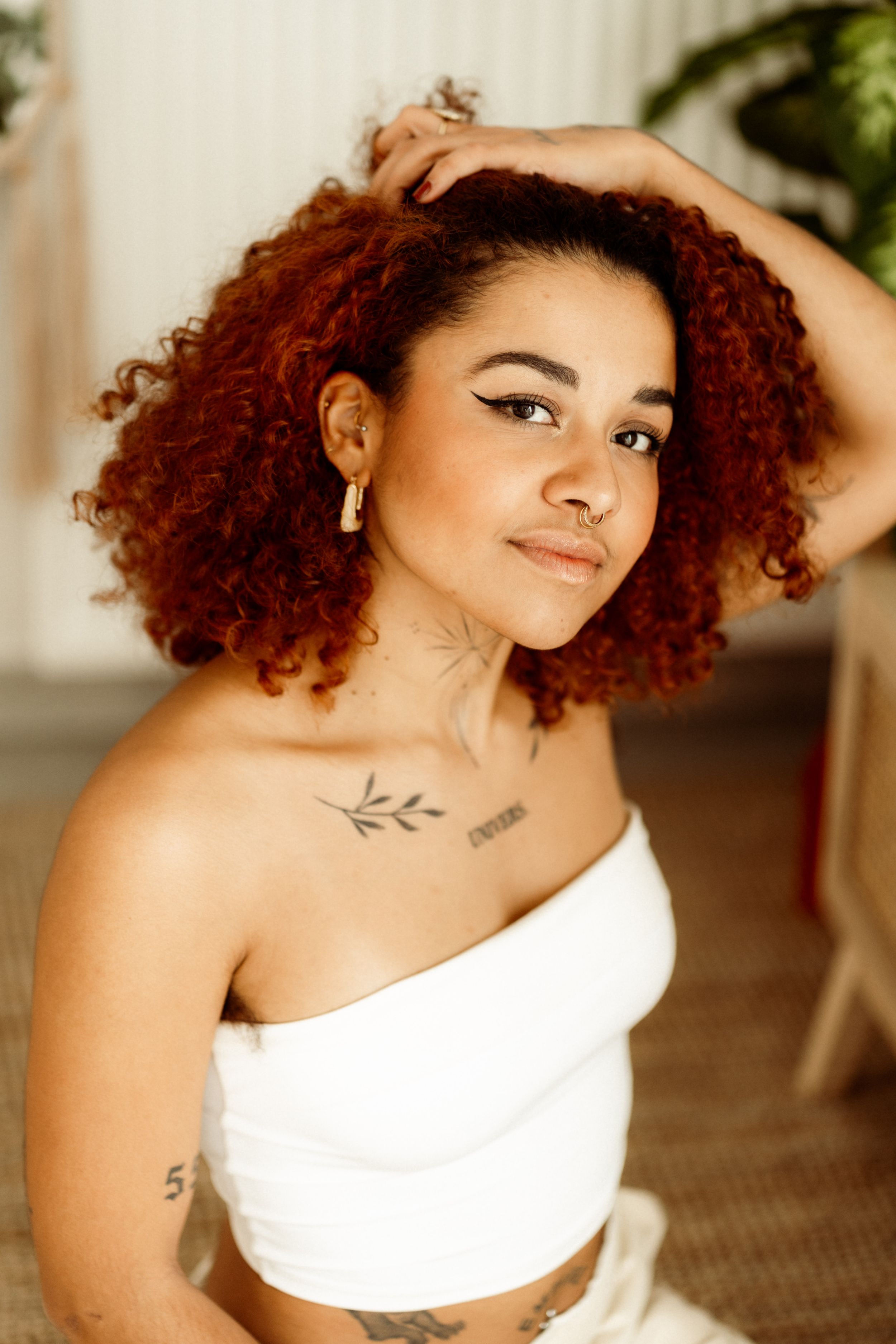 Portrait of photographer with vibrant red curls wearing white crop top and delicate jewelry.