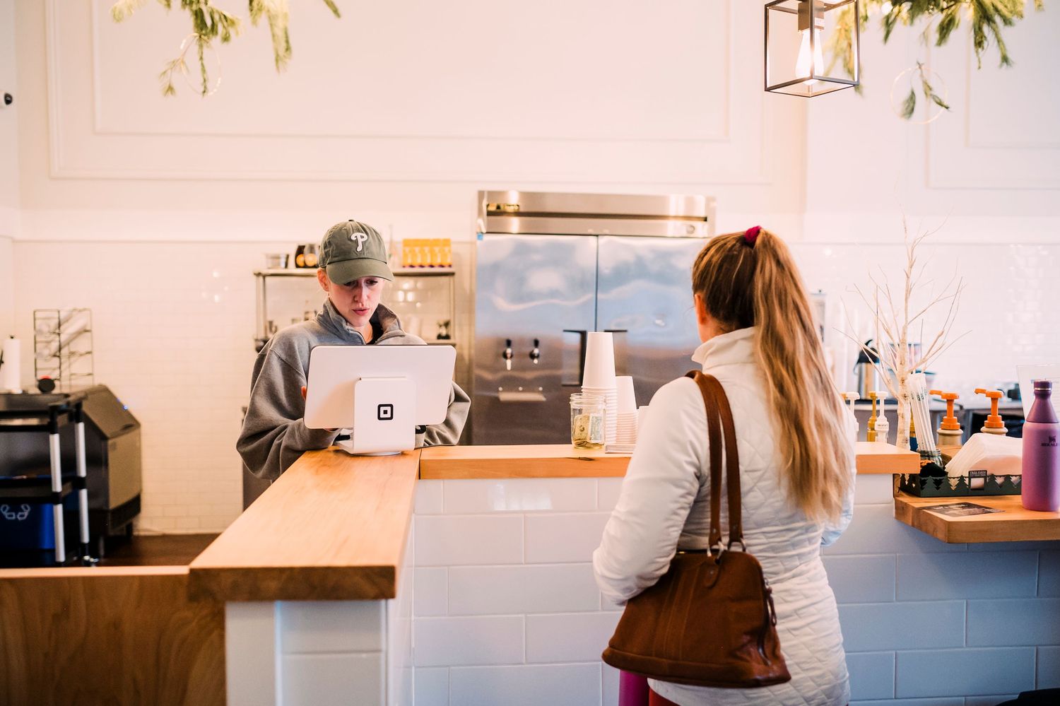 Customer ordering at modern white coffee shop counter with barista.