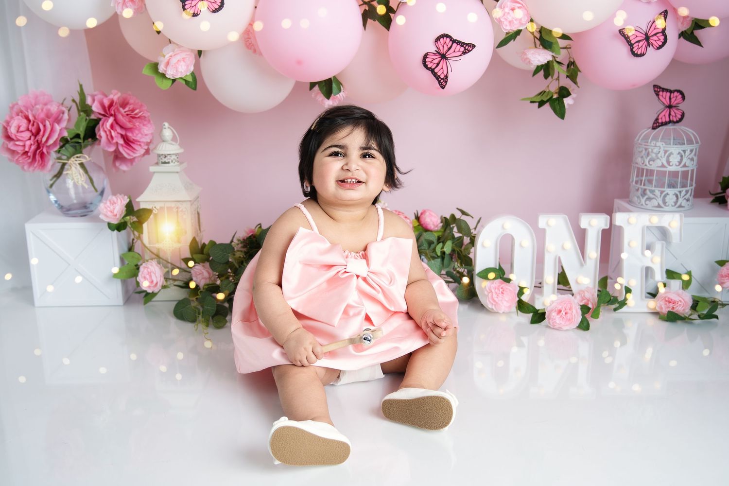 Pink balloon garland with floral accents and white 'ONE' text for birthday photography.