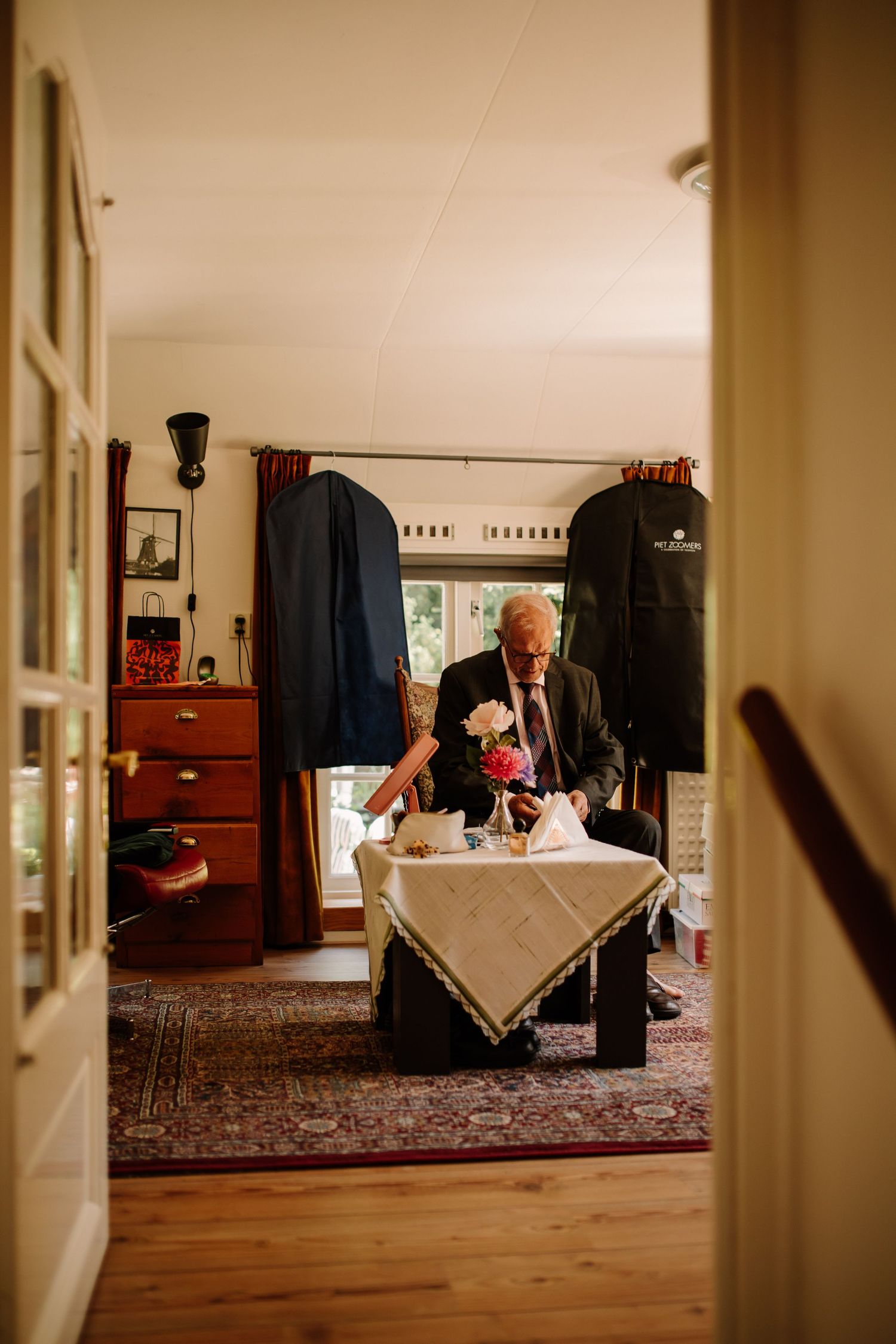 A person seated at a table with garment bags hanging in the background of a cozy room.