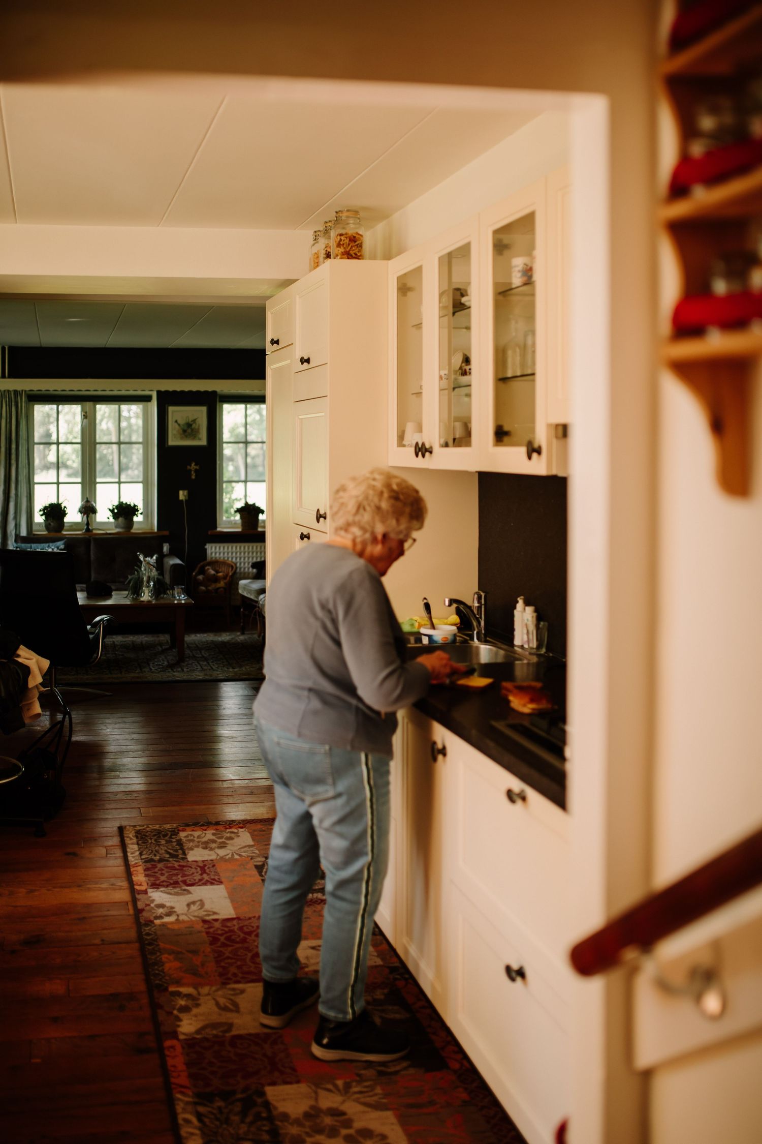 A person working in a bright white kitchen with glass cabinets and hardwood floors.