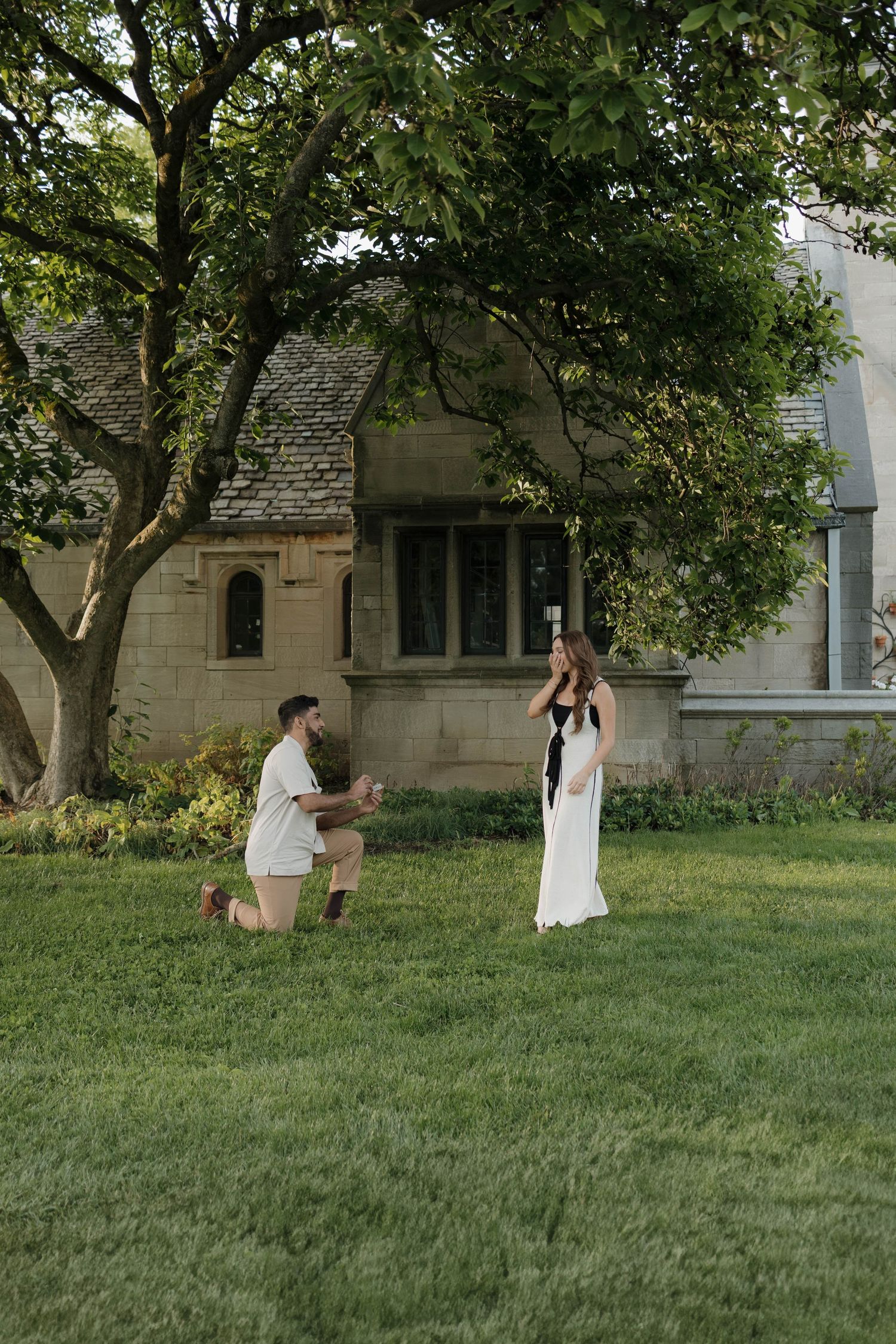 A sequence of photos showing proposal moments on a grassy lawn with trees and a stone building in the background.