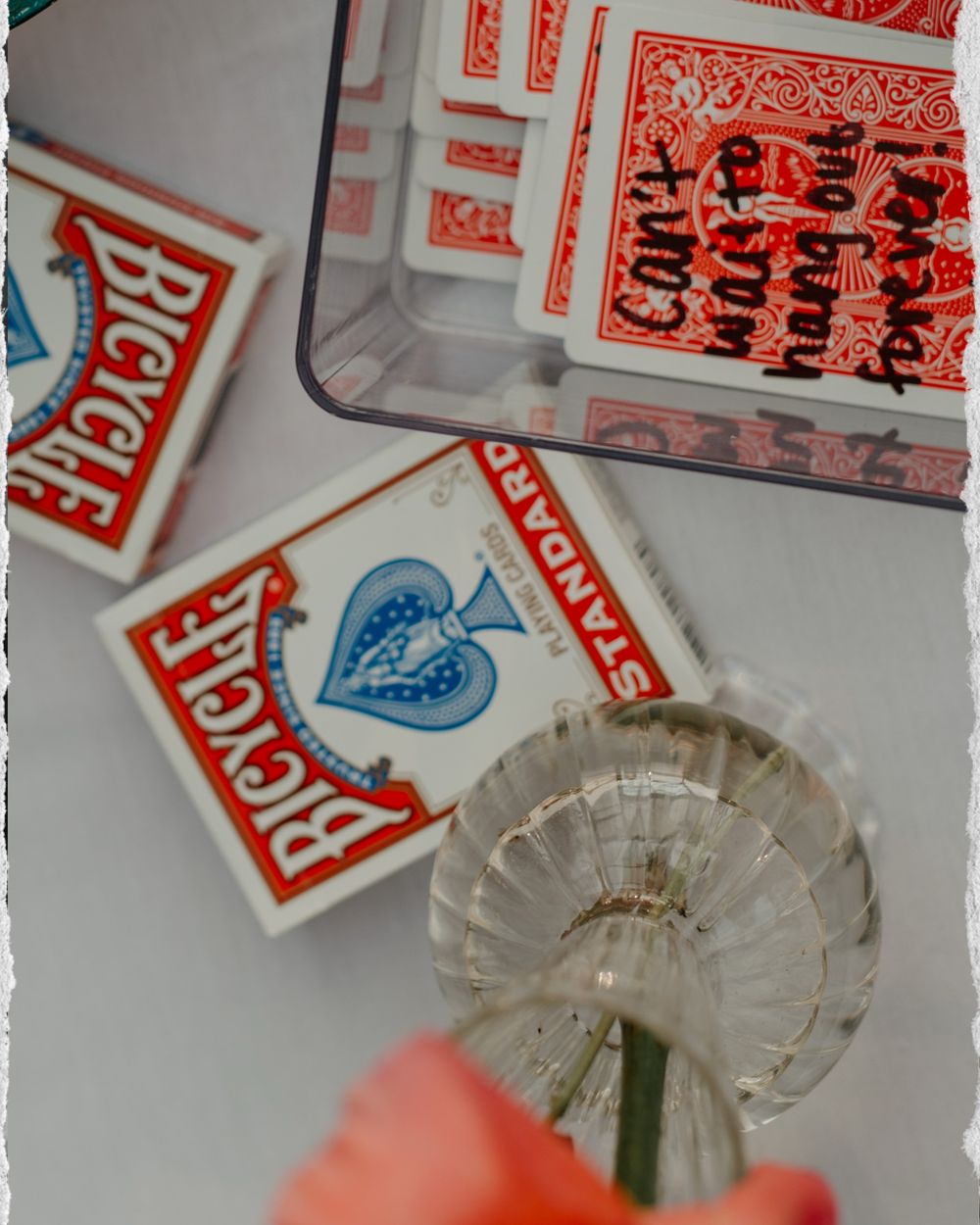 Playing cards and red Bicycle brand card box scattered across a white surface with glass decor.