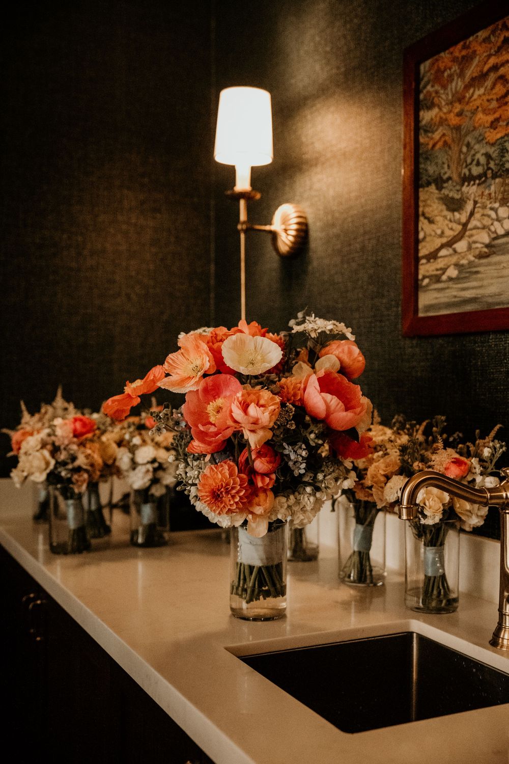 Elegant floral centerpieces with coral roses and white flowers on dark tables with ambient lighting.