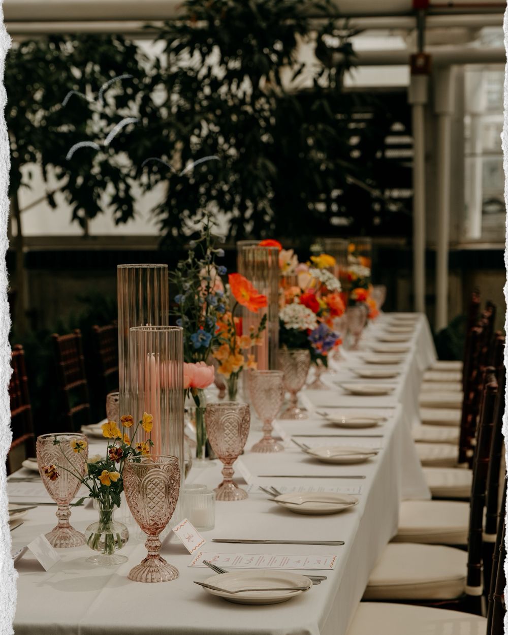 An elegant table setting at a wedding reception with crystal glasses and orange floral centerpieces.