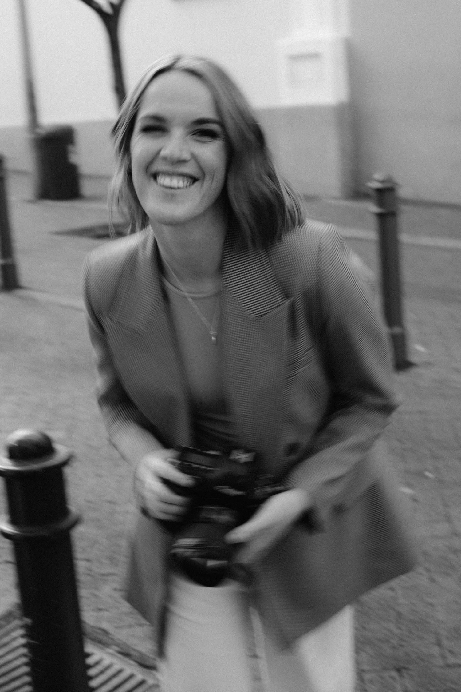 A person in a blazer holds a camera while smiling outdoors.