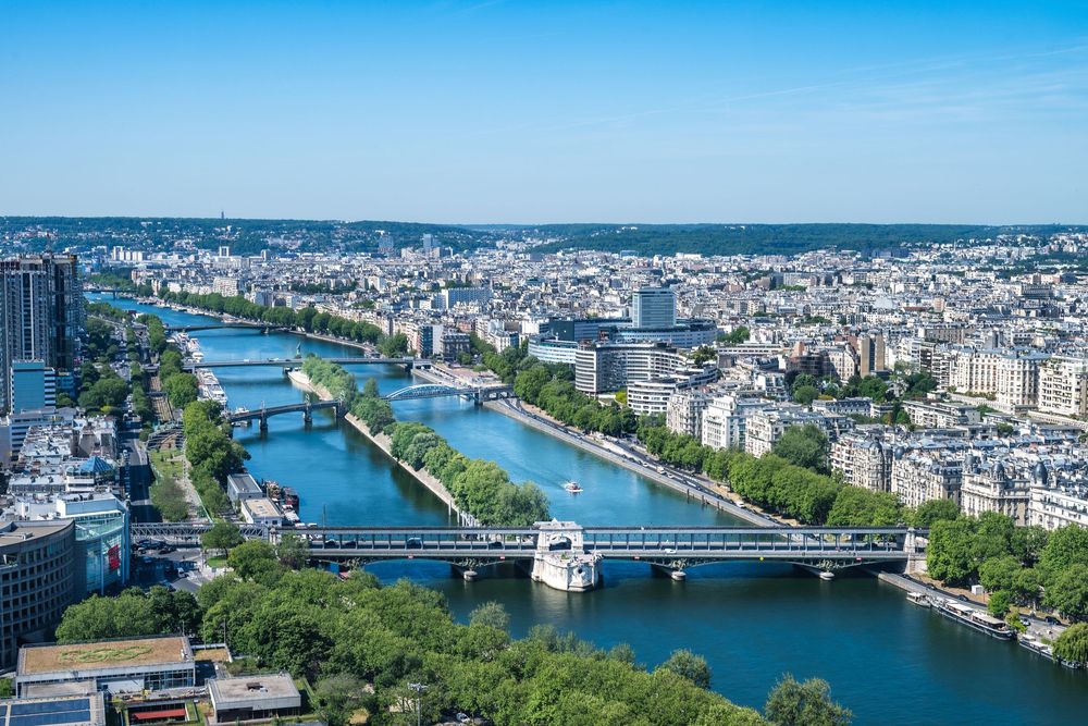 Aerial panoramic view of Paris with the Seine River winding through the city and multiple bridges crossing the waterway.