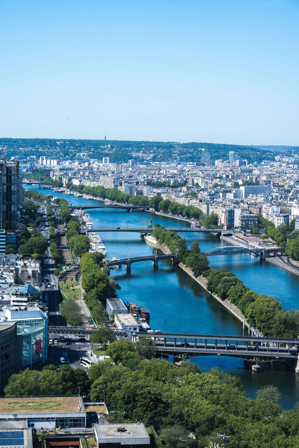 Aerial view of multiple bridges crossing the Seine River in Paris with tree-lined riverbanks and urban cityscape.