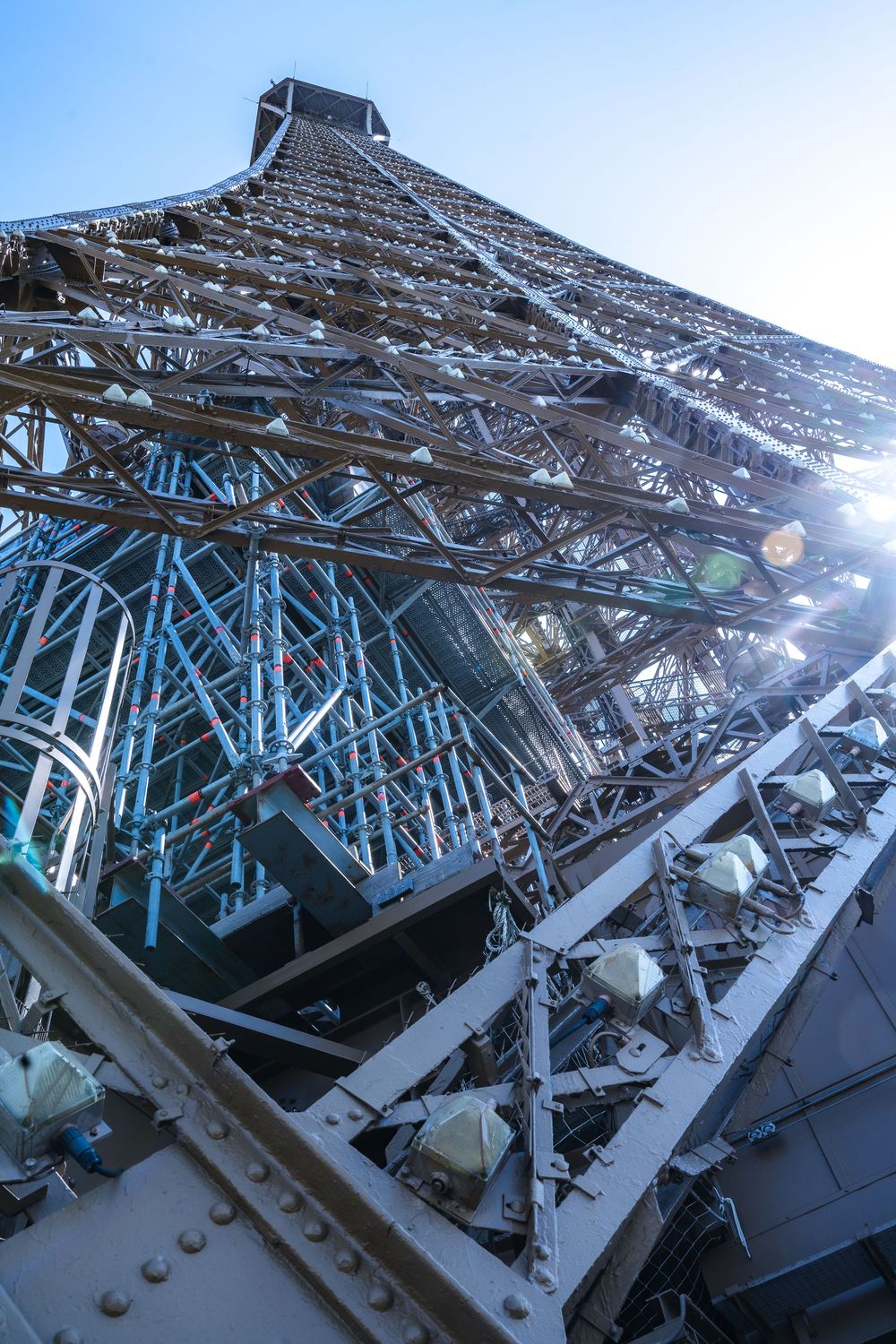 Looking up at the Eiffel Tower's iron lattice structure from below with sunlight shining through the metalwork.