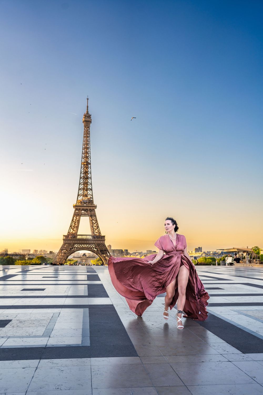 A flowing mauve dress billows in front of the Eiffel Tower at Trocadero square during golden sunset in Paris.