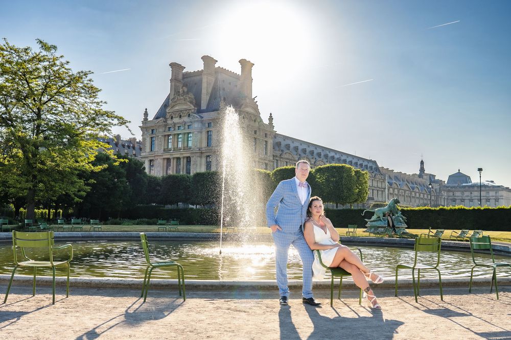 Two individuals pose together on a sunny day in front of a fountain at the Tuileries Garden in Paris.