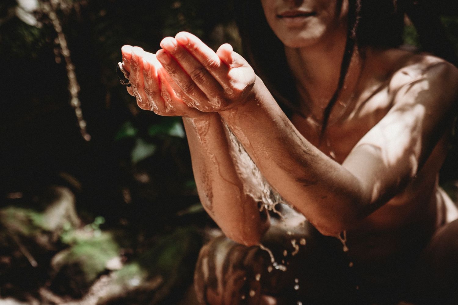 Mulher nua em sessão fotográfica feminina na natureza foto colorida com braços na agua em momento de coneXão com a natureza