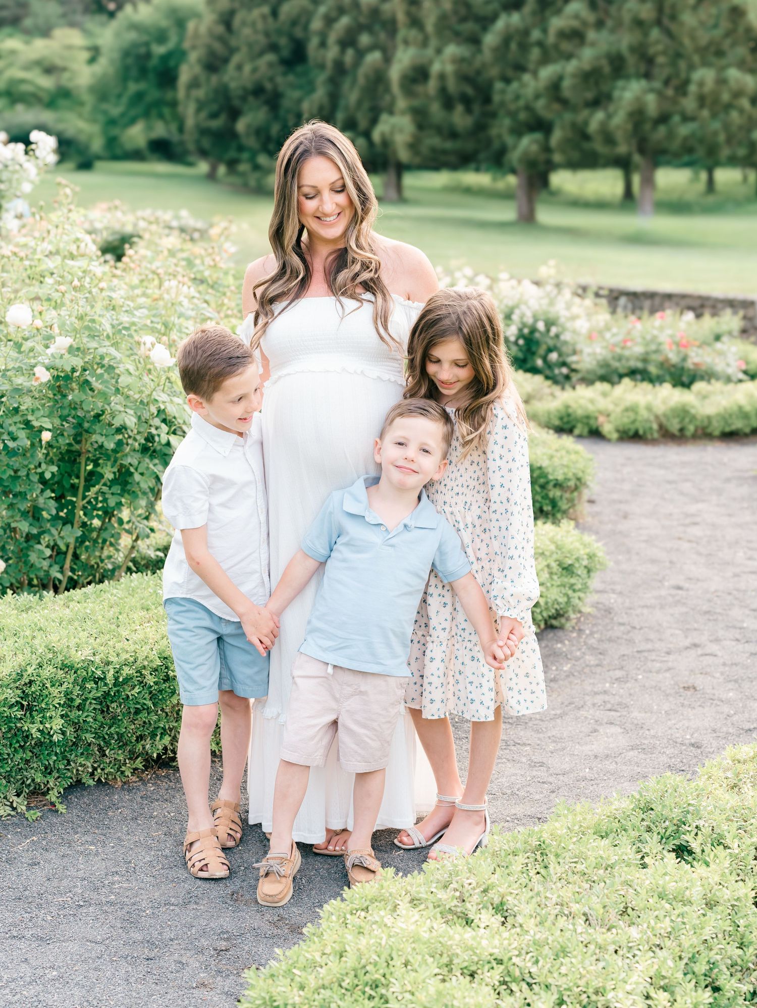 Pregnant mother in a flowing white dress smiling with her partner and child in a lush garden setting.