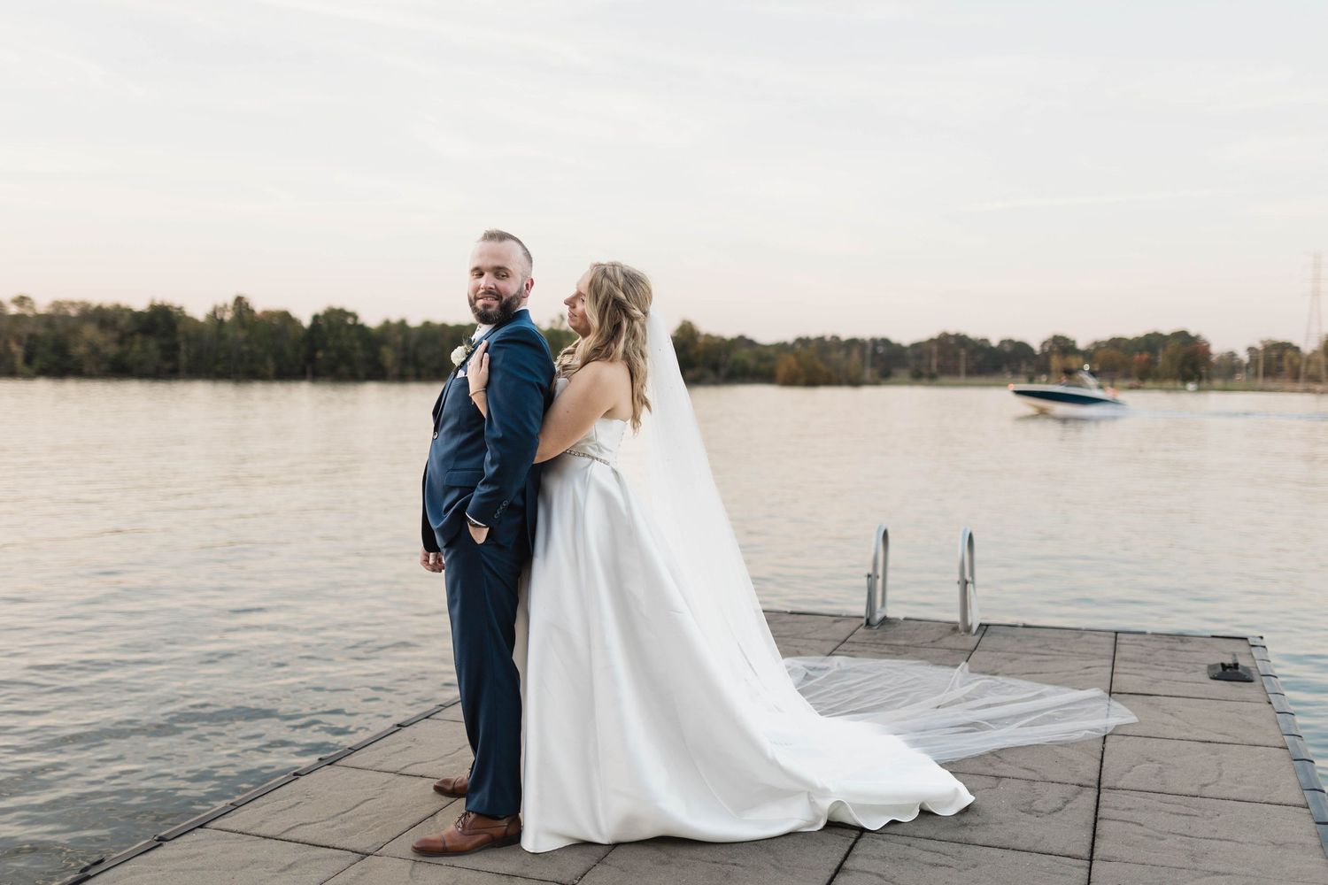 A couple in wedding attire shares a joyful moment together on a dock by the water at sunset.