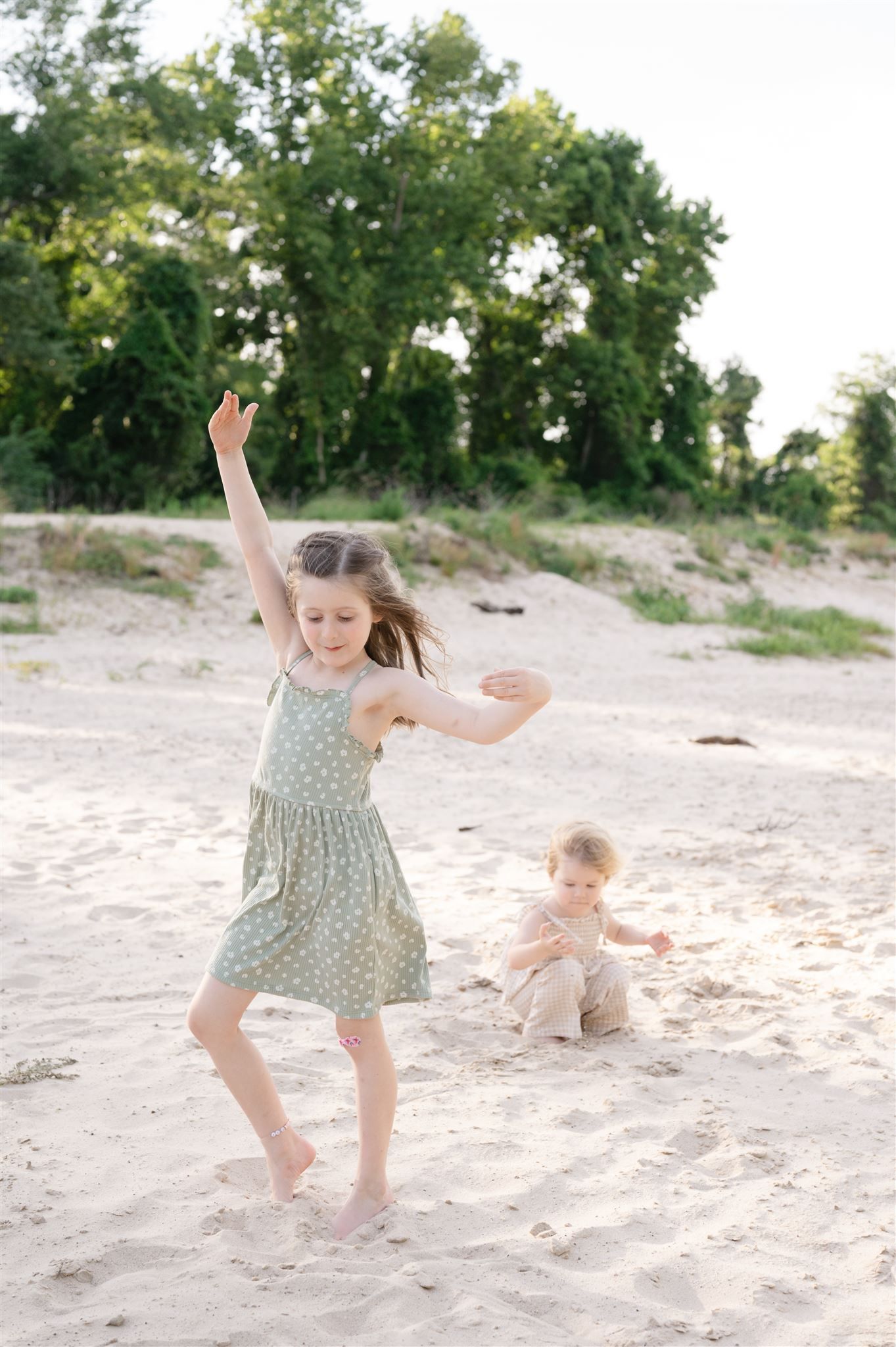 Two children playing and jumping on a sandy beach with trees in the background on a sunny day.
