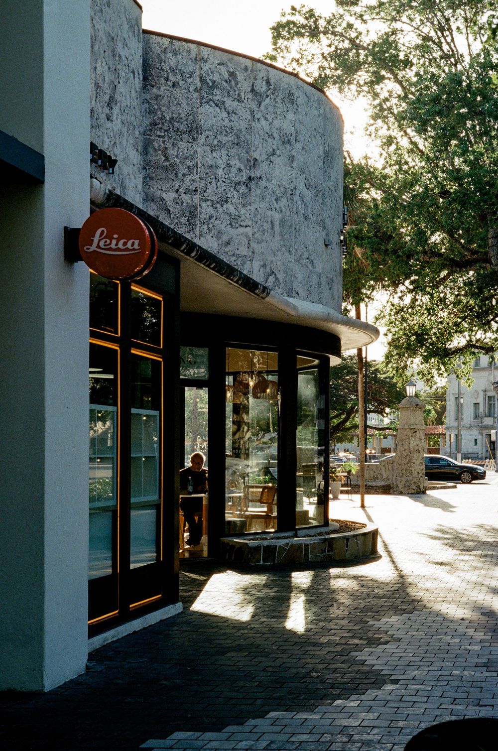 A vintage-style Leica camera store storefront with curved architecture and brick pavement on a sunny afternoon.