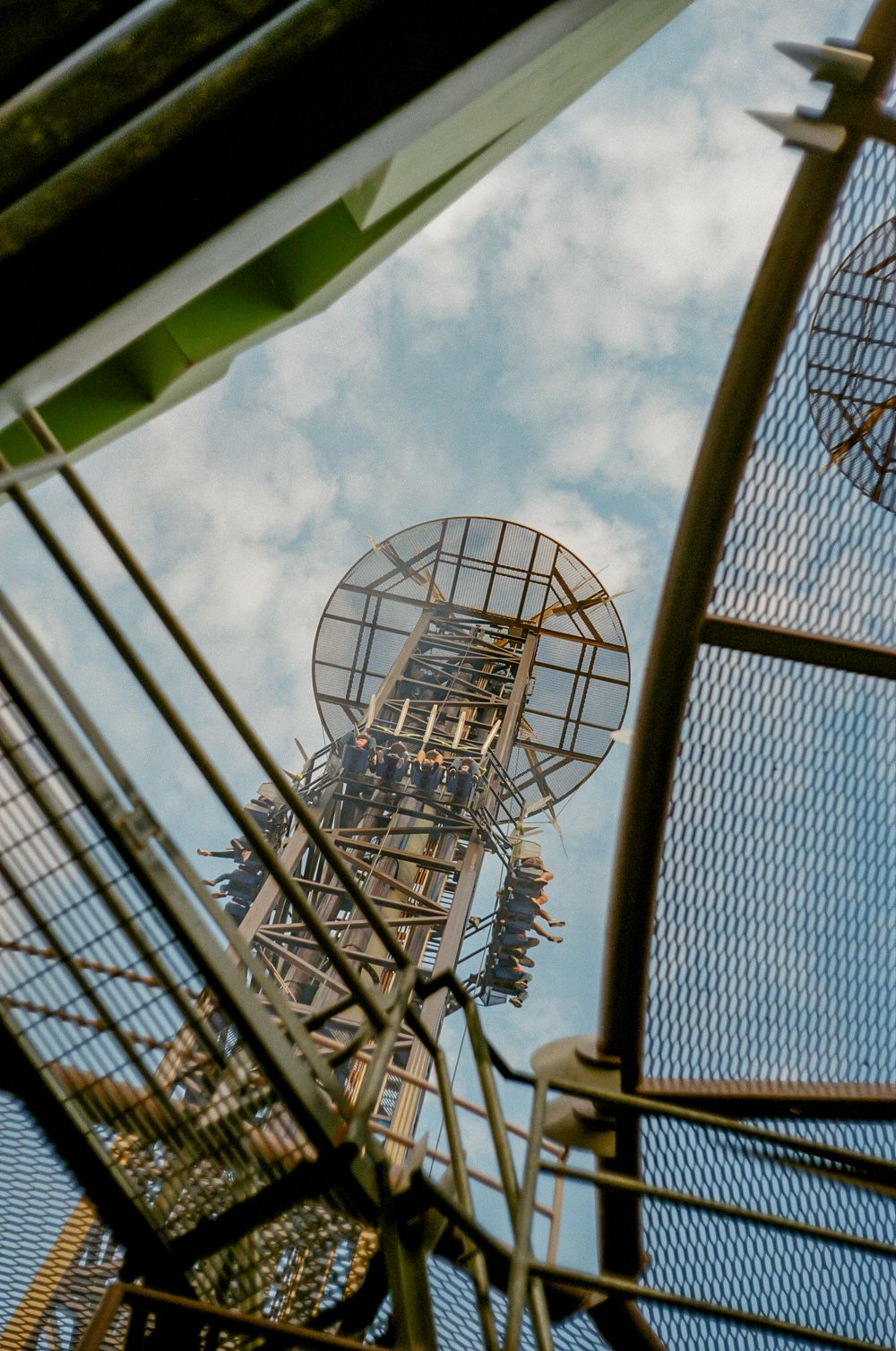 A tall industrial tower with a spherical metal grid structure photographed from below against a cloudy blue sky.