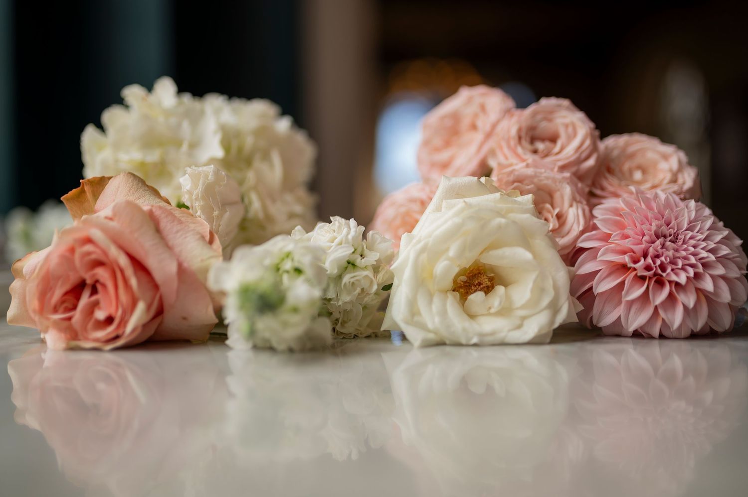 Delicate arrangement of pink and white roses with dahlias on reflective surface.